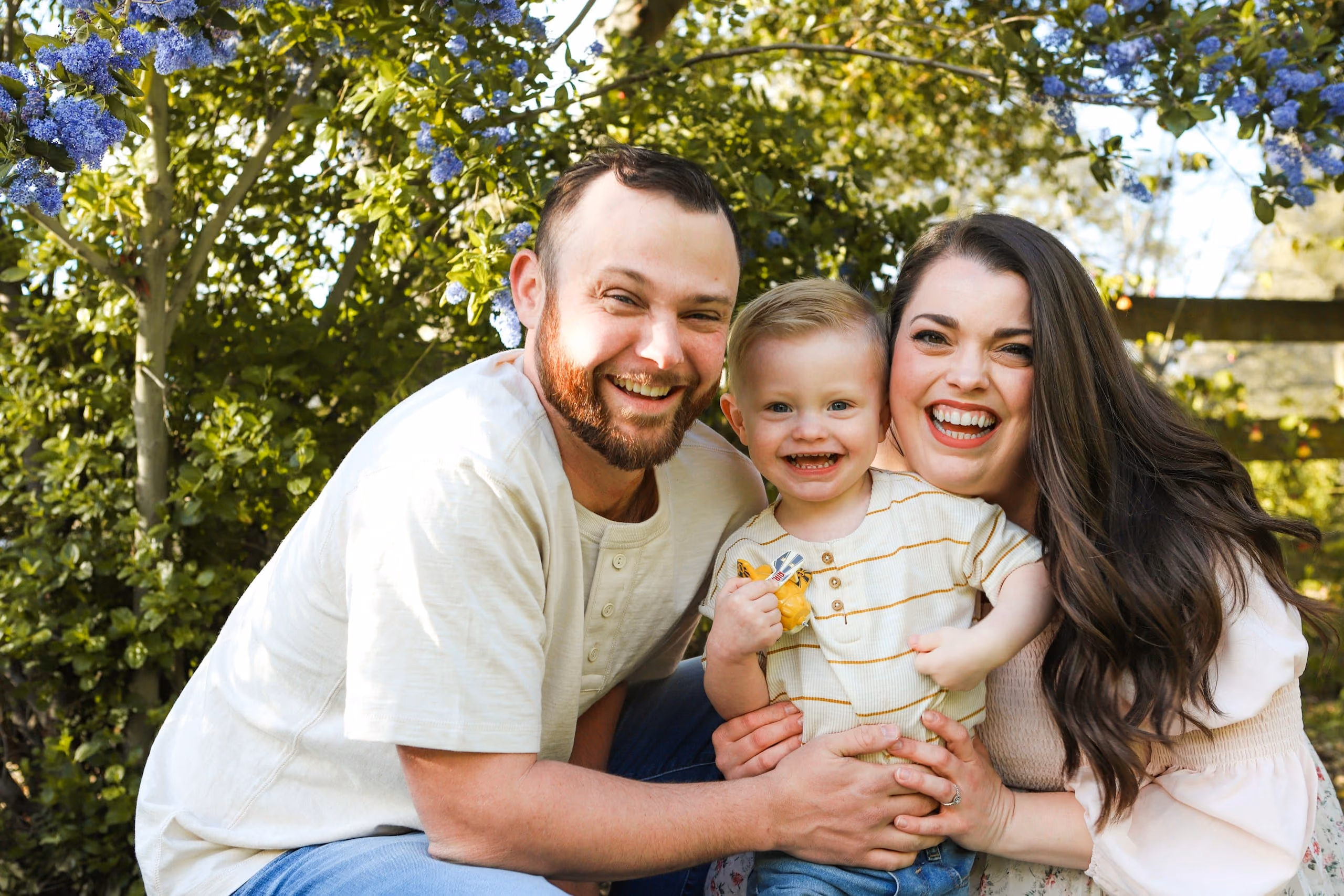 Parents hugging their smiling toddler in a sunny garden