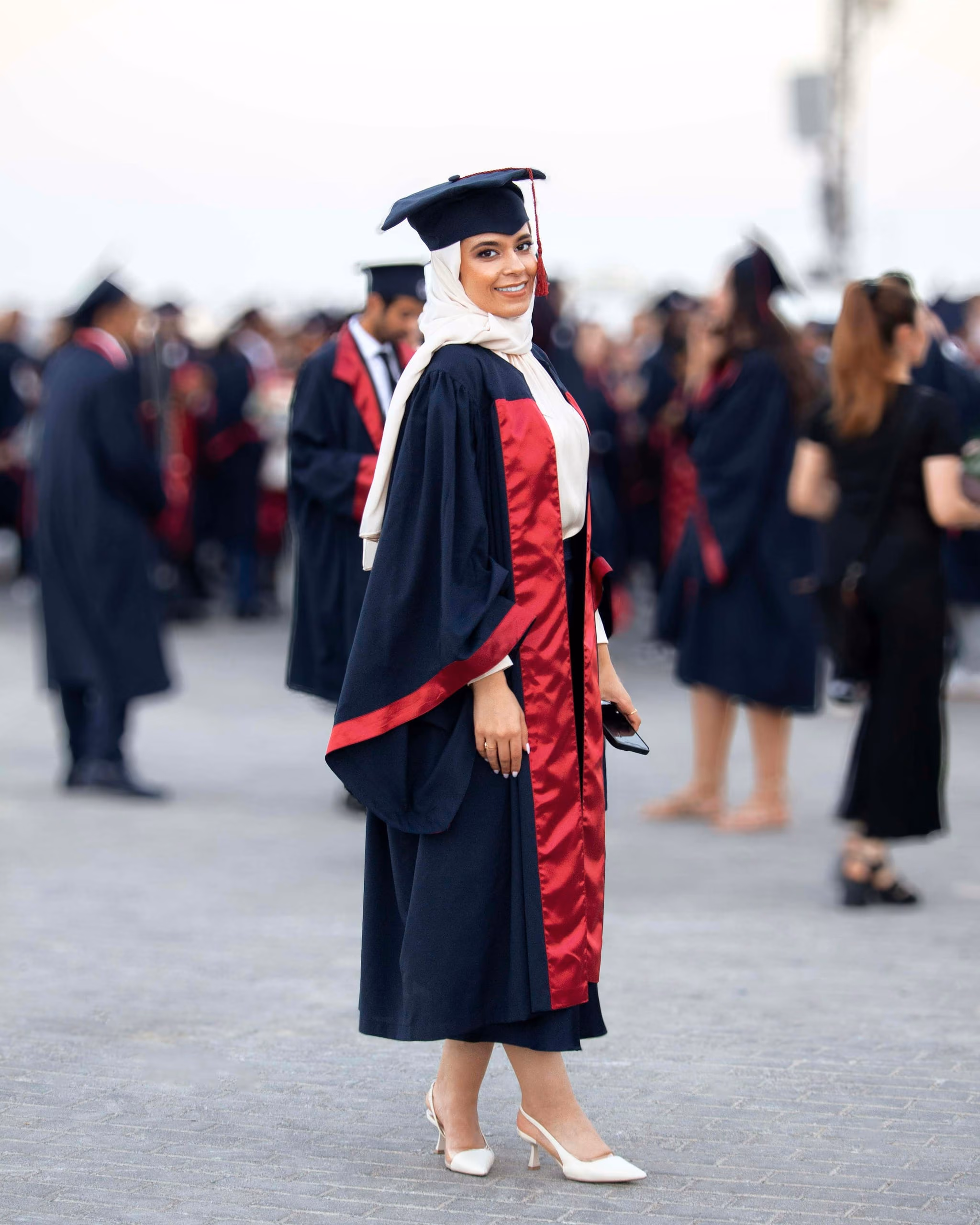 A graduate in hijab, gown and red stole standing among her classmates