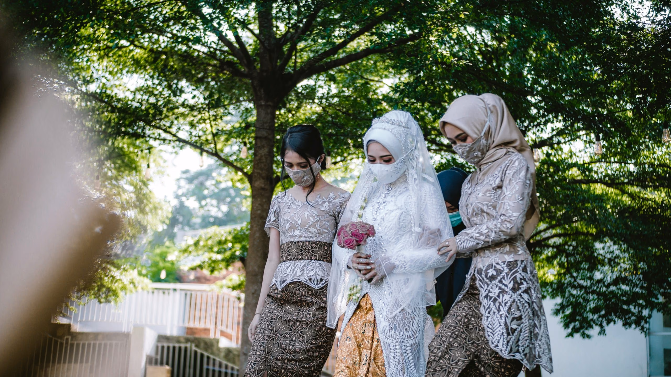 A bride in white walking under a tree with two women from her family