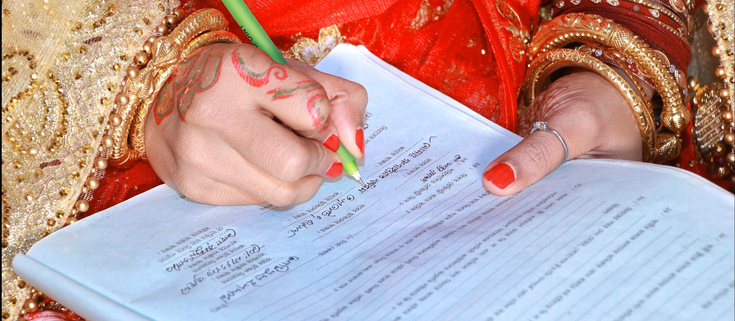 A bride's henna-decorated hand signing the nikkah contract