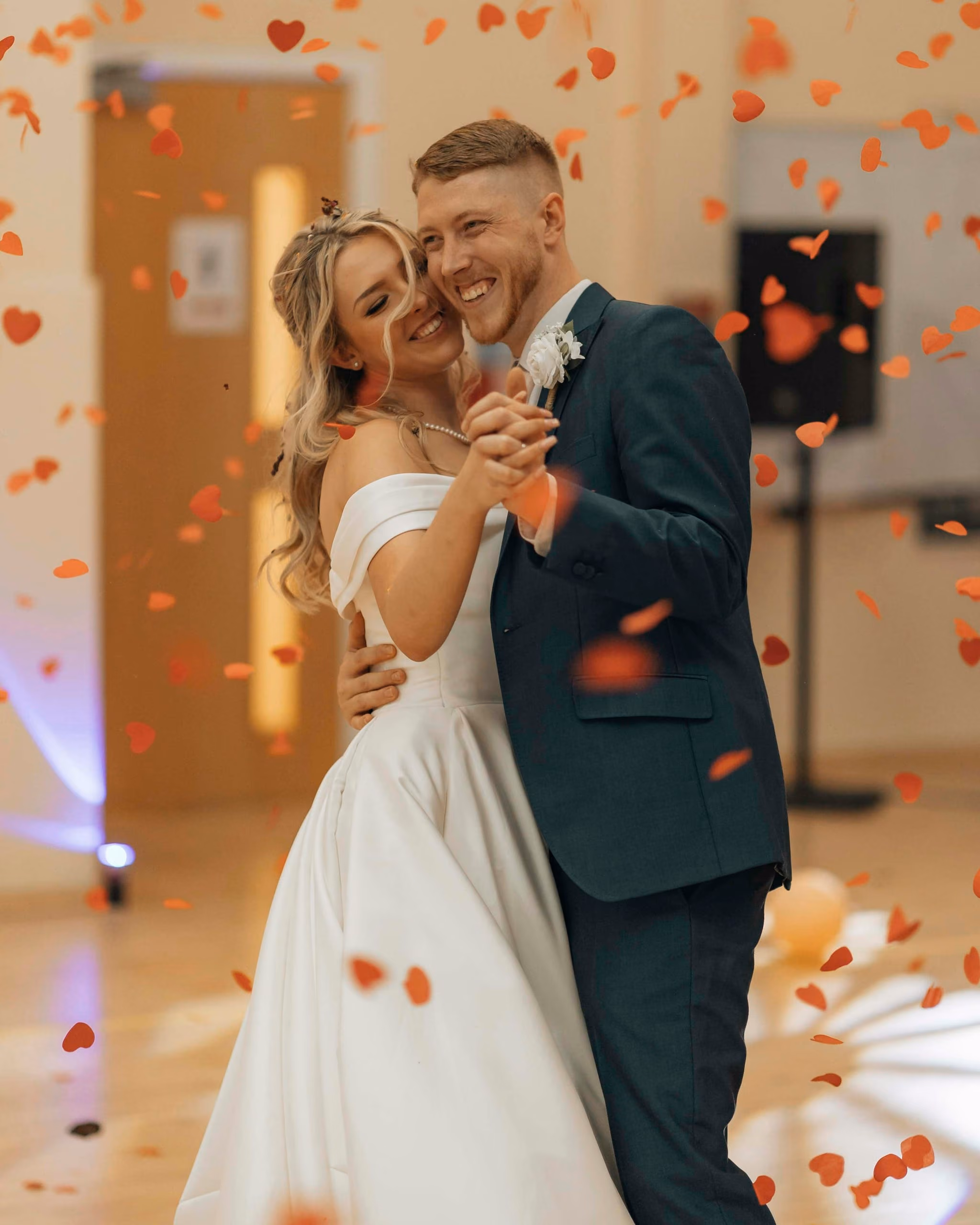 A bride and groom smiling during their first dance as petals fall
